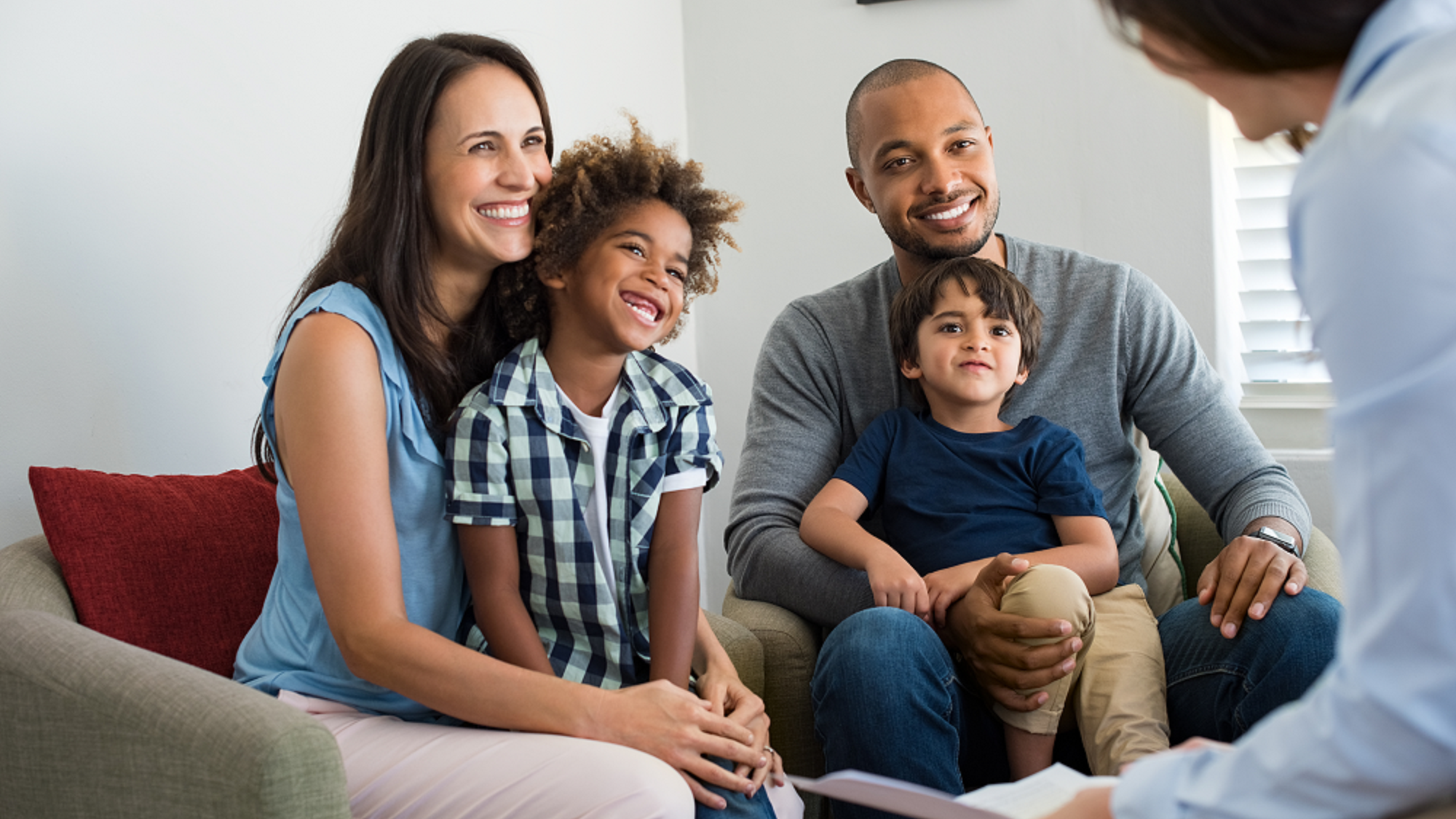 family therapy session with mum and dad and two young boys sons sitting on sofa smiling at therapist