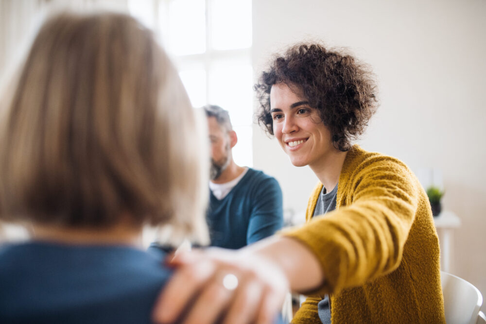 Woman in mental health therapy putting arm on other woman's shoulder