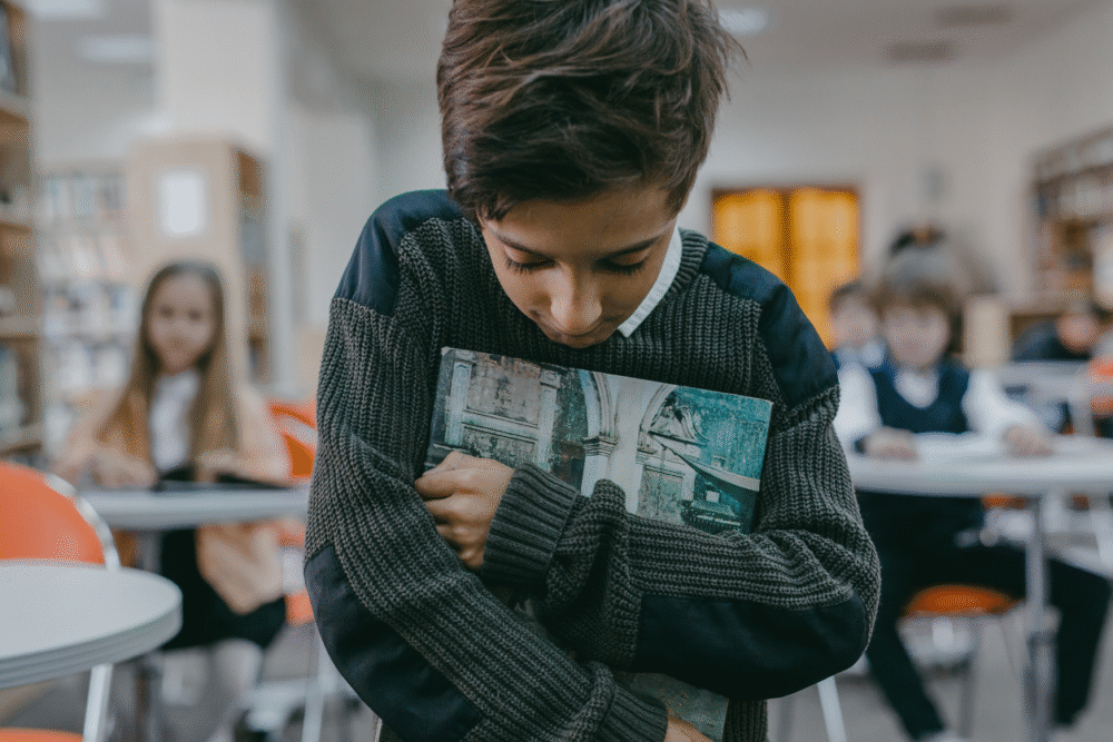 Child grabbing book looking down and upset walking through a classromm