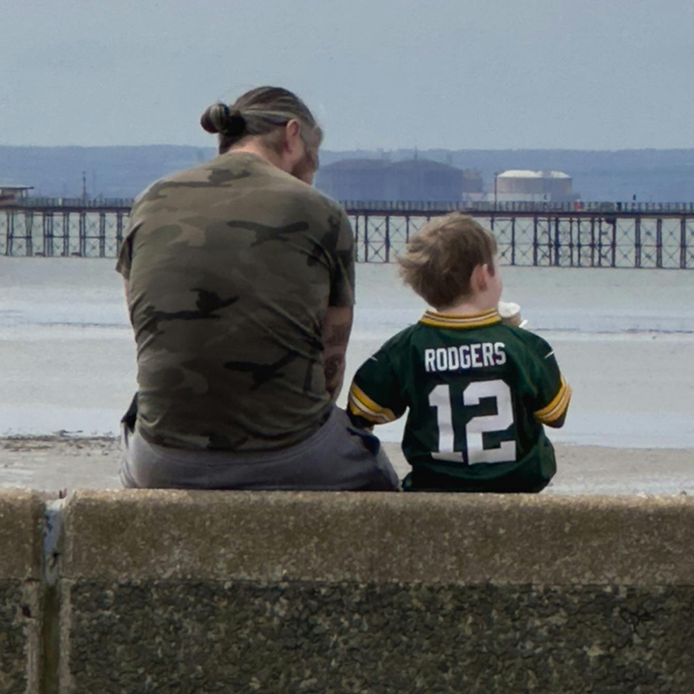 Man and child sat on a wall looking to sea