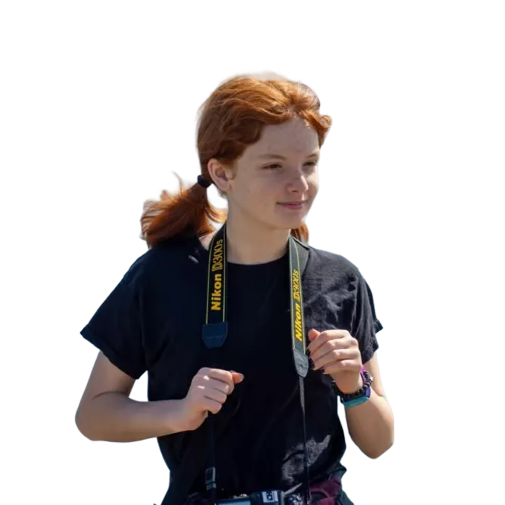 Redheaded teen photographer in black t-shirt holding a Nikon camera with yellow Nikon strap