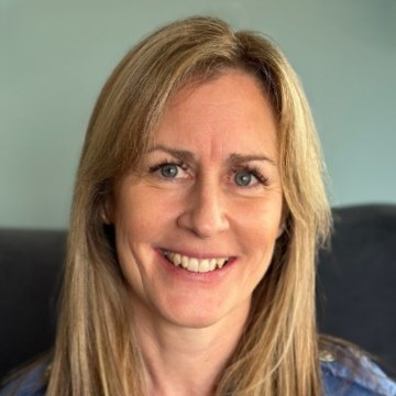 Close-up professional headshot of smiling blonde woman with long hair and neutral background.