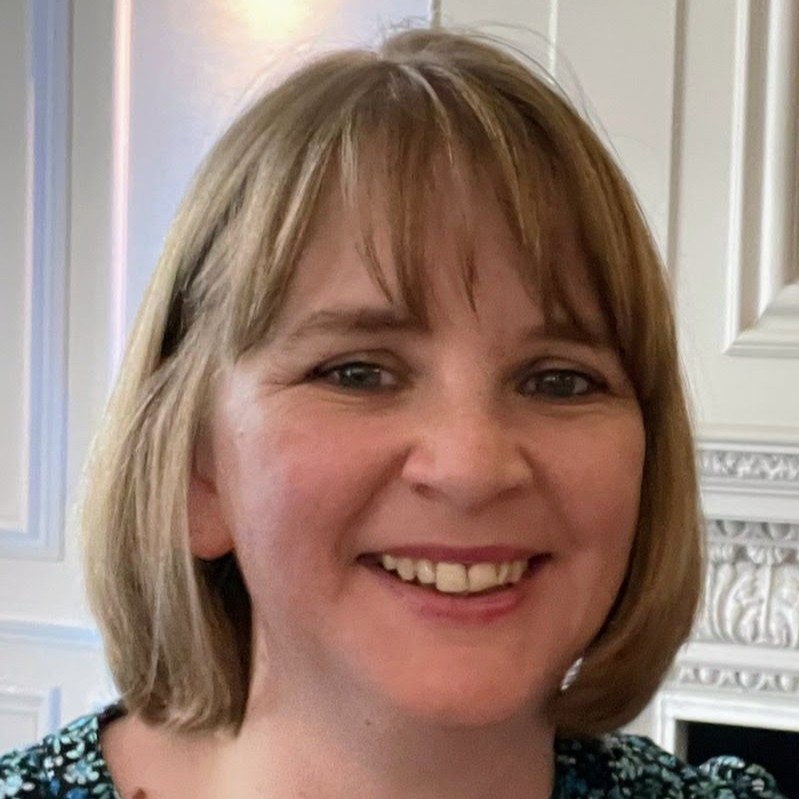 Close-up portrait of a friendly smiling woman with short blonde hair in a bright, ornate white interior