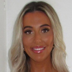 Portrait of smiling woman with long wavy blonde hair, tan skin, polished makeup and glossy pink lips against white background